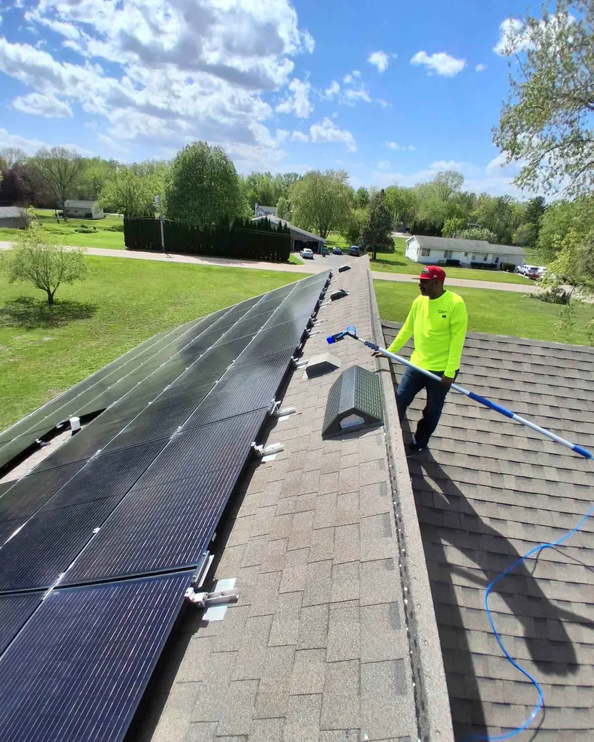 Jesse on the roof working a solar array with a long-reach water-fed pole and soft brush head