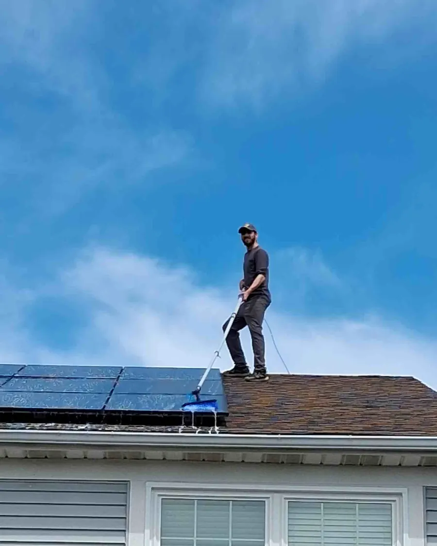 Jesse on a roof working a solar array with a long-reach water-fed pole